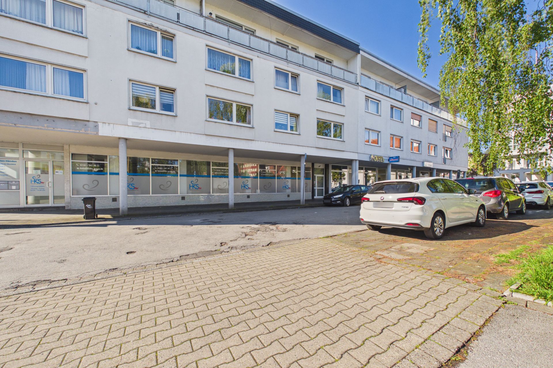 Dreistöckiges Wohnhaus mit weißen Fassaden und geparkten Autos davor bei Tageslicht.