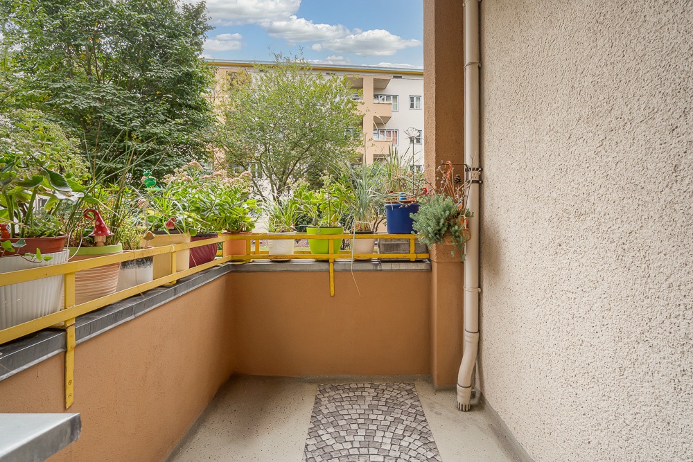 Balkon mit vielen Pflanzentöpfen auf dem Geländer und Blick auf Bäume und ein Wohngebäude.