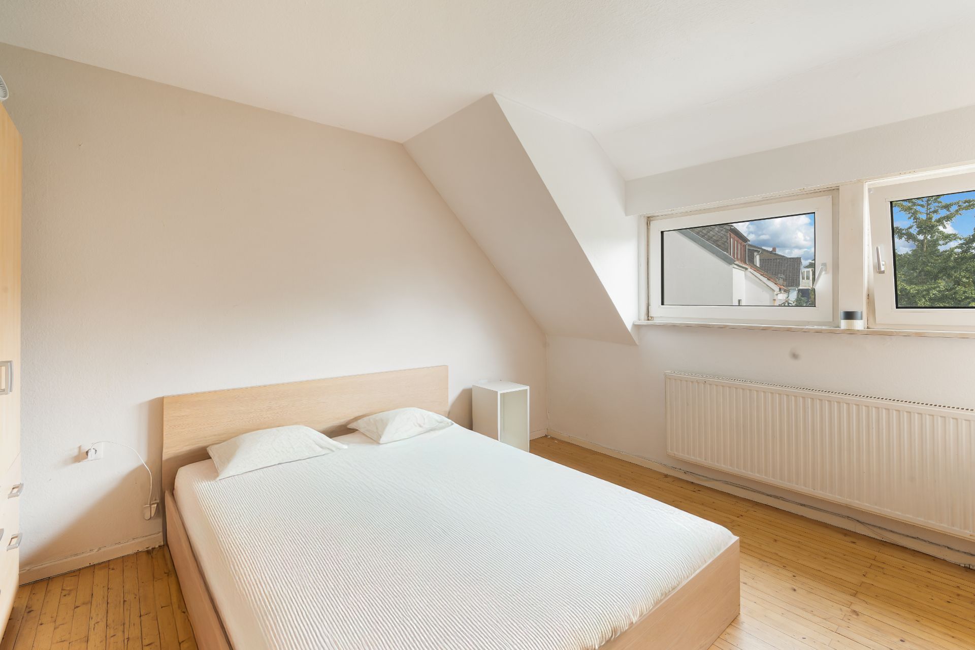 Helles Schlafzimmer mit Doppelbett, Holzfußboden und zwei Fenstern an der Wand.