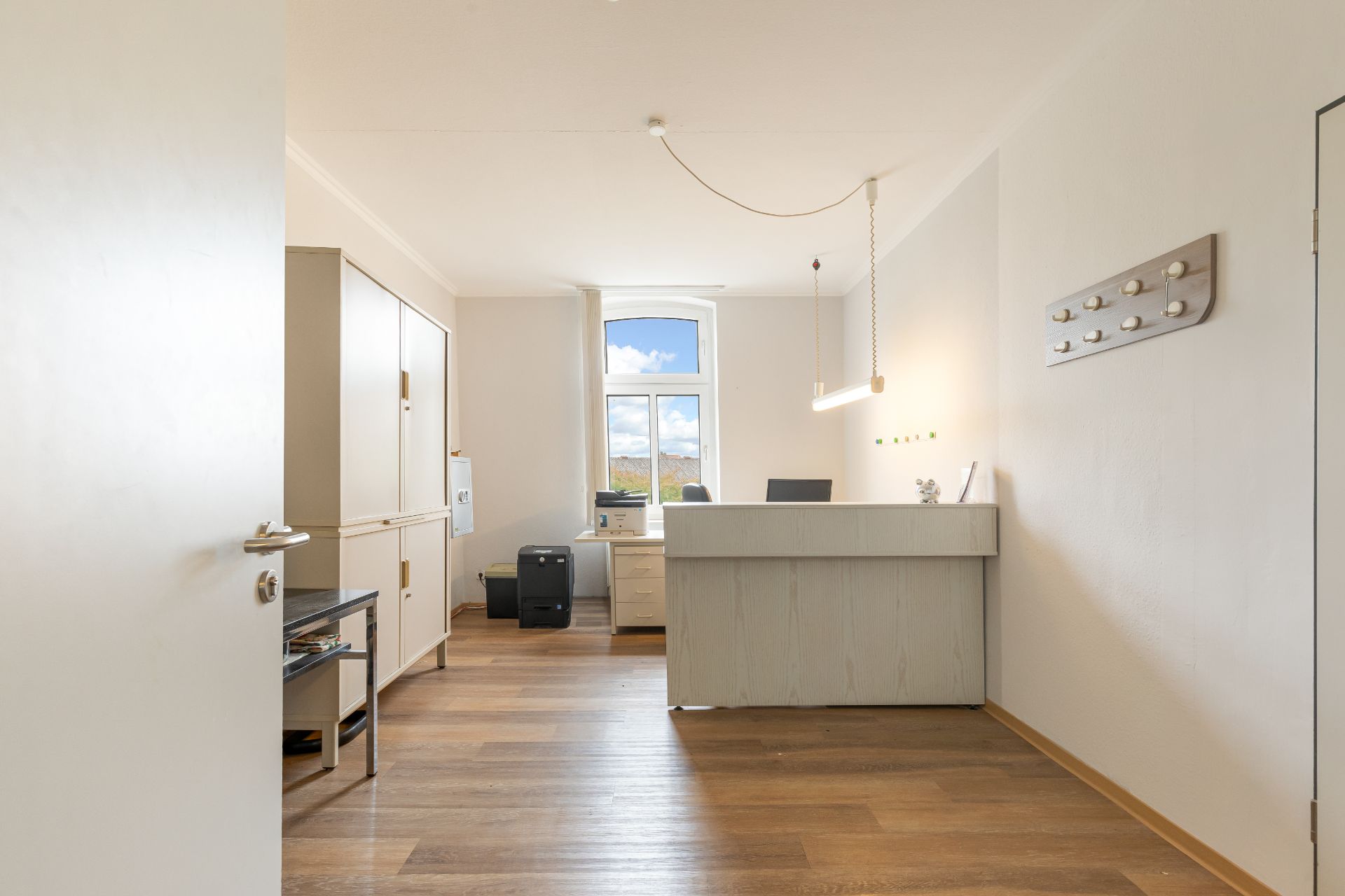 Helles Arbeitszimmer mit Schreibtisch, Stuhl und großem Fenster, Holzfußboden.