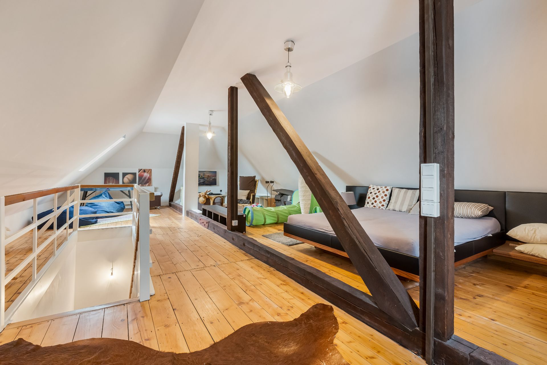 Dachgeschosszimmer mit Holzboden, Doppelbett, Sitzbereich und sichtbaren Holzbalken.