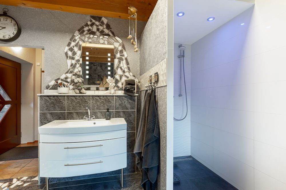Modernes Badezimmer mit Waschbecken, Spiegel, Handtüchern und offener Dusche mit Beleuchtung.