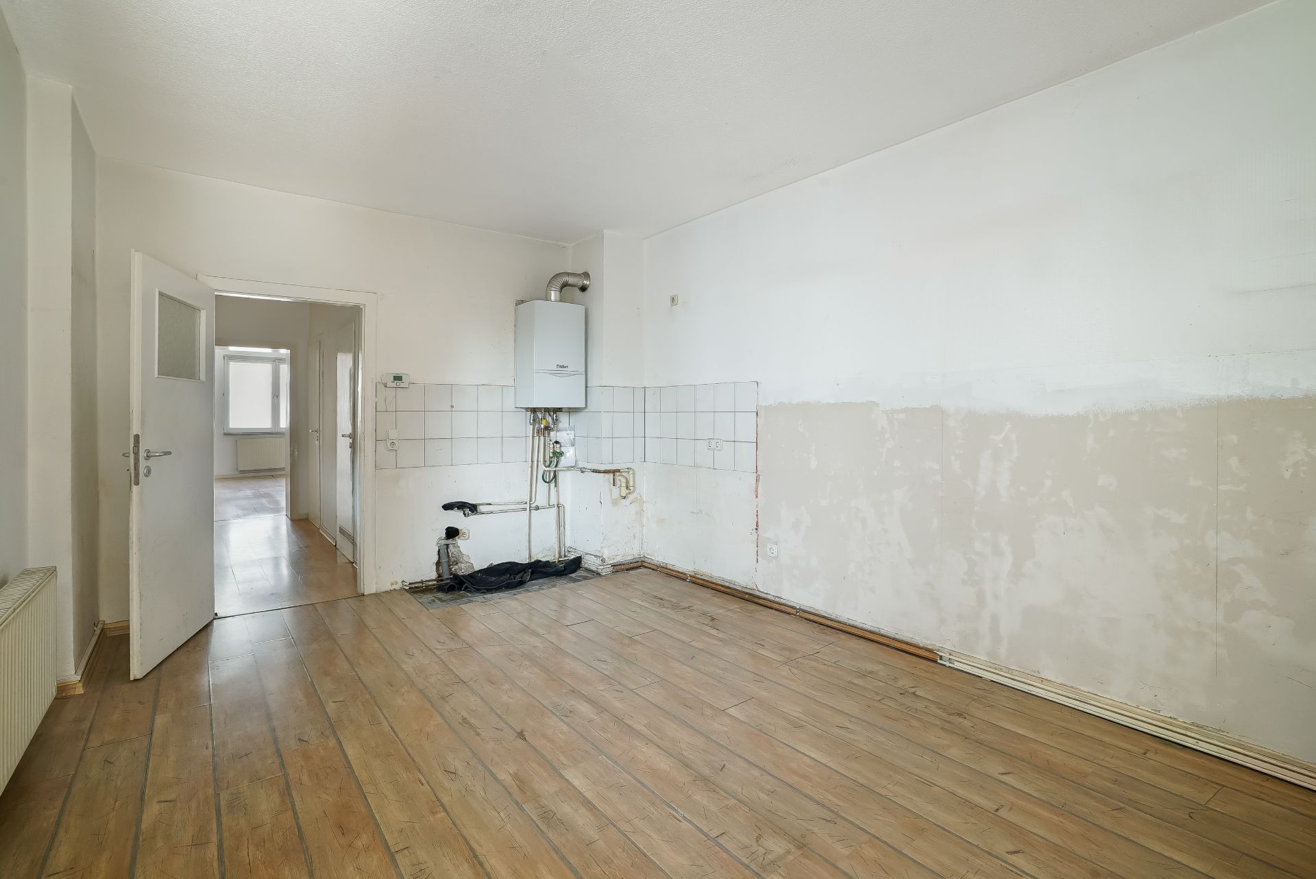 Leerer Raum mit Holzboden, weißen Wänden und Gastherme an der Wand.