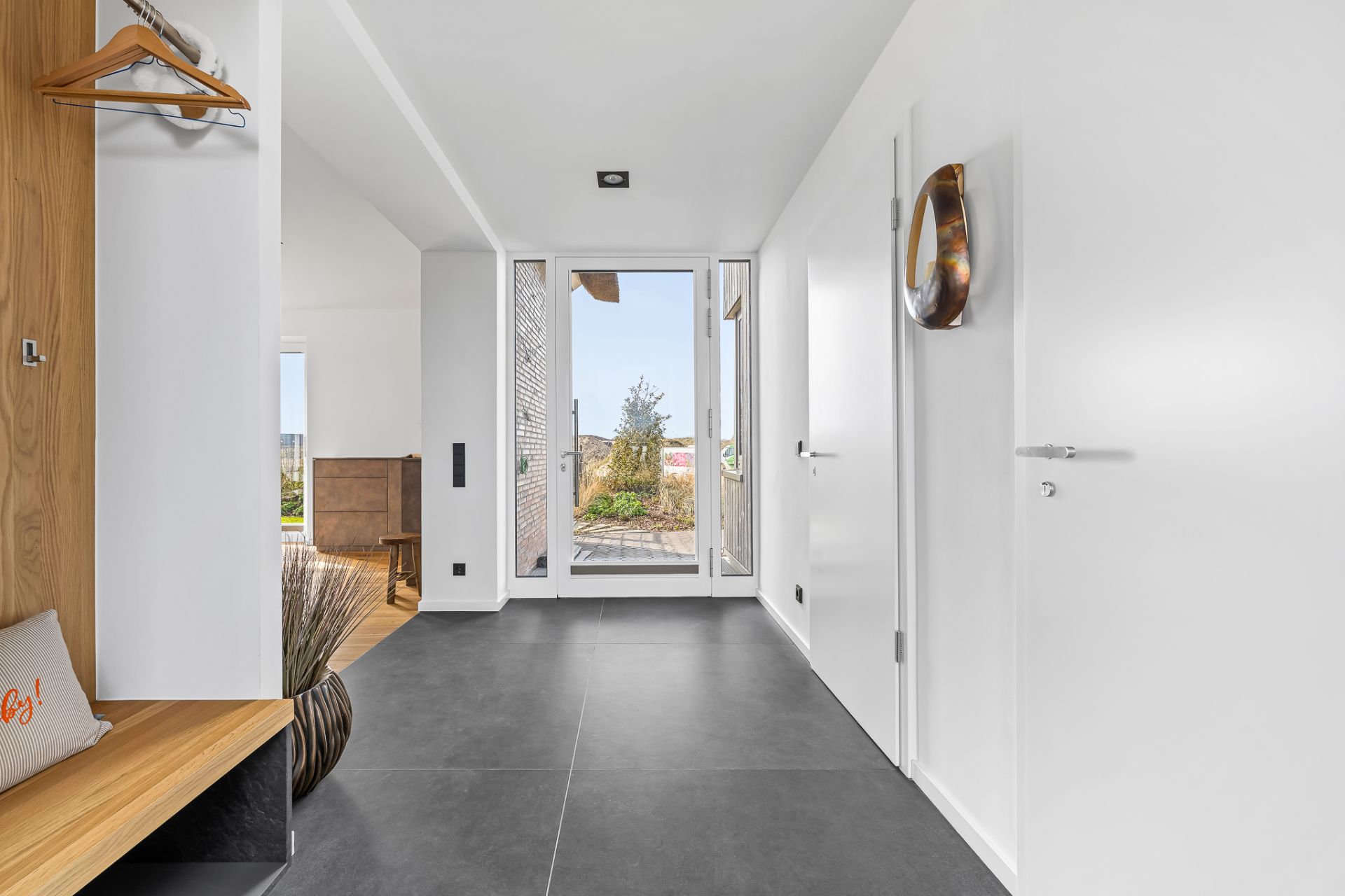 Heller Flur mit großen Fliesen, Holzgarderobe und Glastür zum Garten.