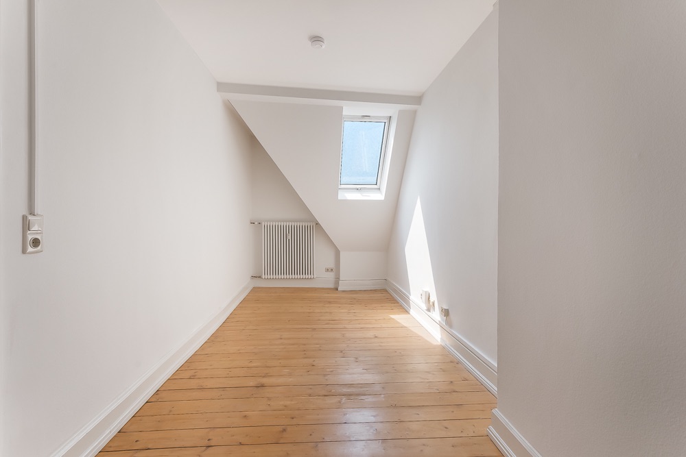 Heller Raum mit schräger Decke, Holzboden, Heizkörper und Fenster im Dach.
