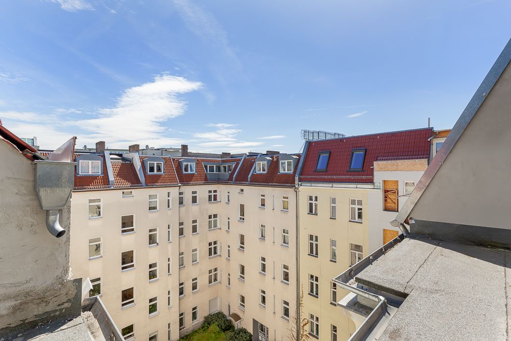 Blick auf einen hellen Innenhof mit Mehrfamilienhäusern und roten Dächern unter blauem Himmel.