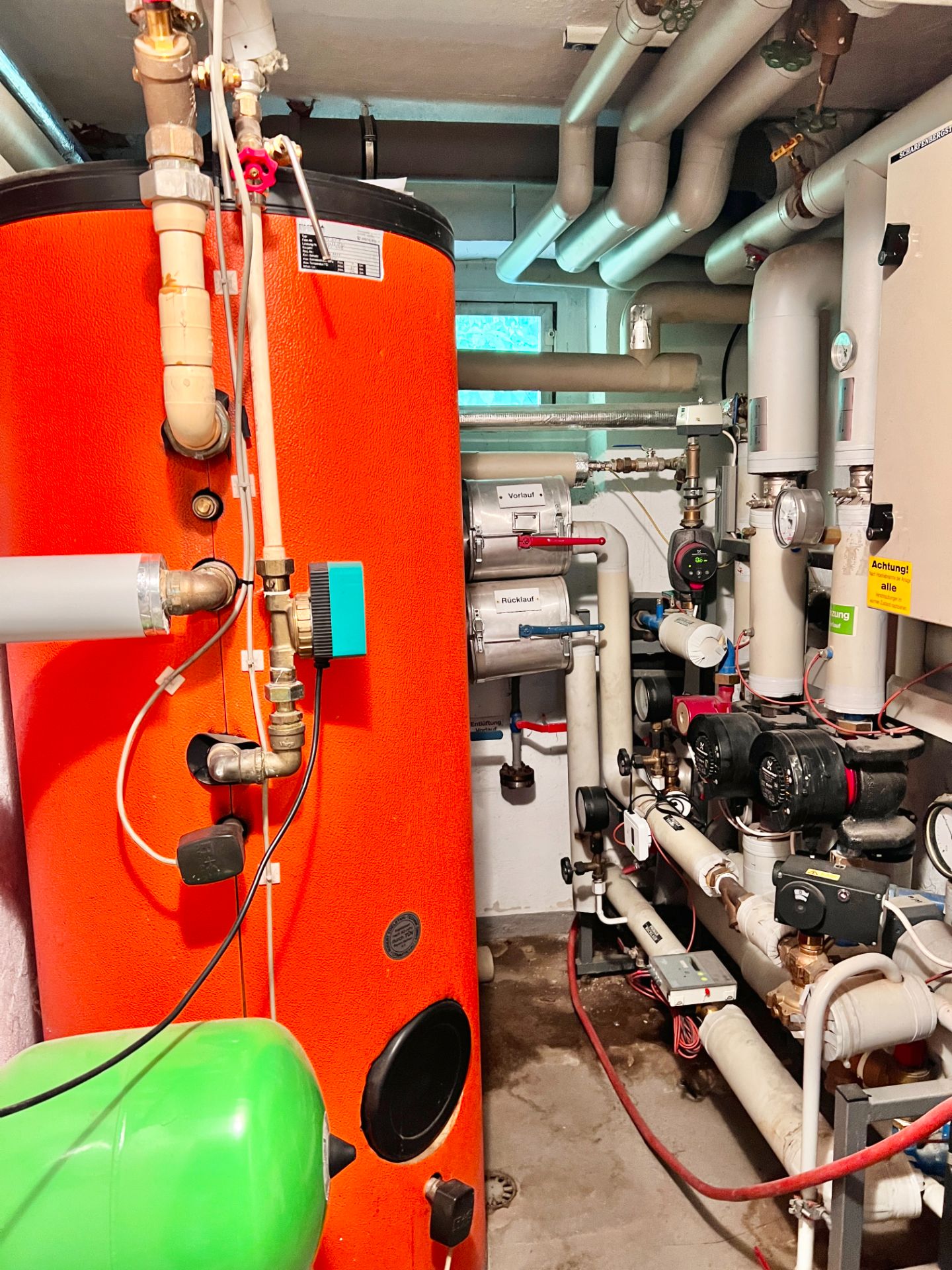 Heizungsraum mit orangefarbenem Boiler, Rohren und technischen Anlagen.