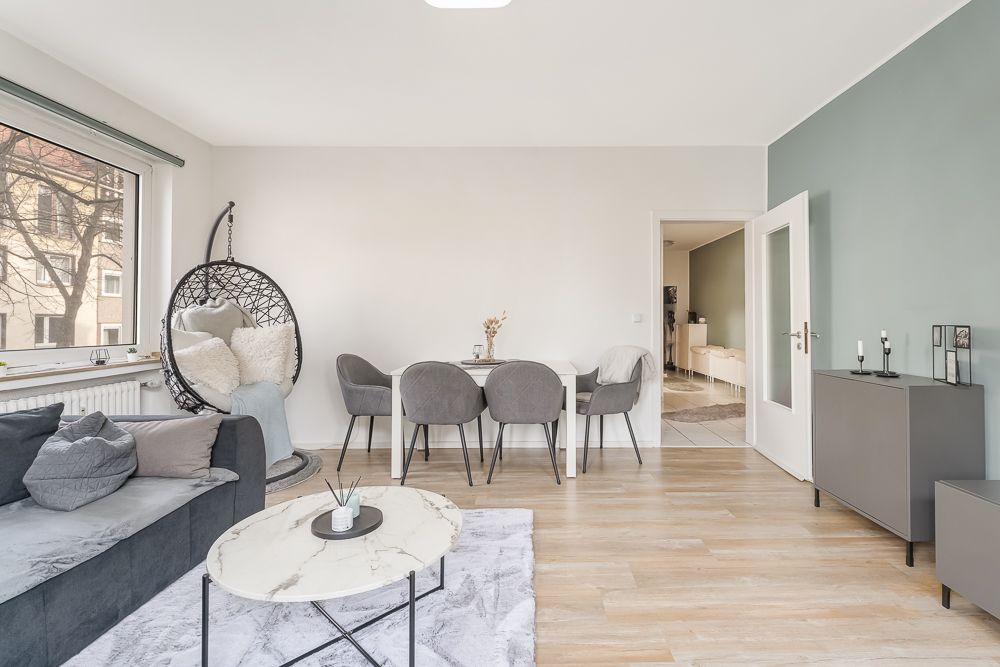 Modernes Wohnzimmer mit grauem Sofa, Esstisch, Hängesessel und großem Fenster.