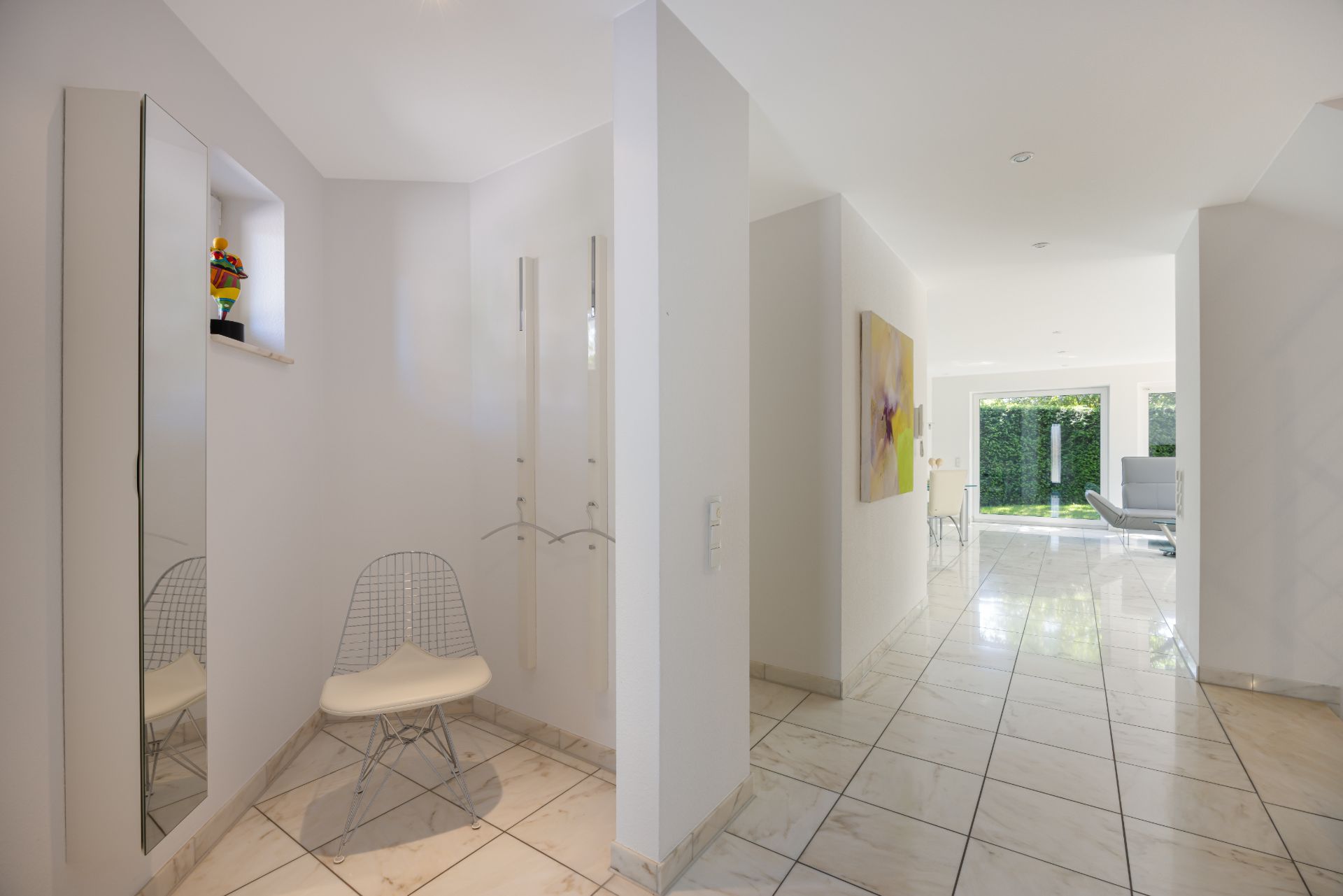 Heller Flur mit Spiegel, Stuhl, Garderobe und Blick in ein Wohnzimmer mit großen Fenstern.
