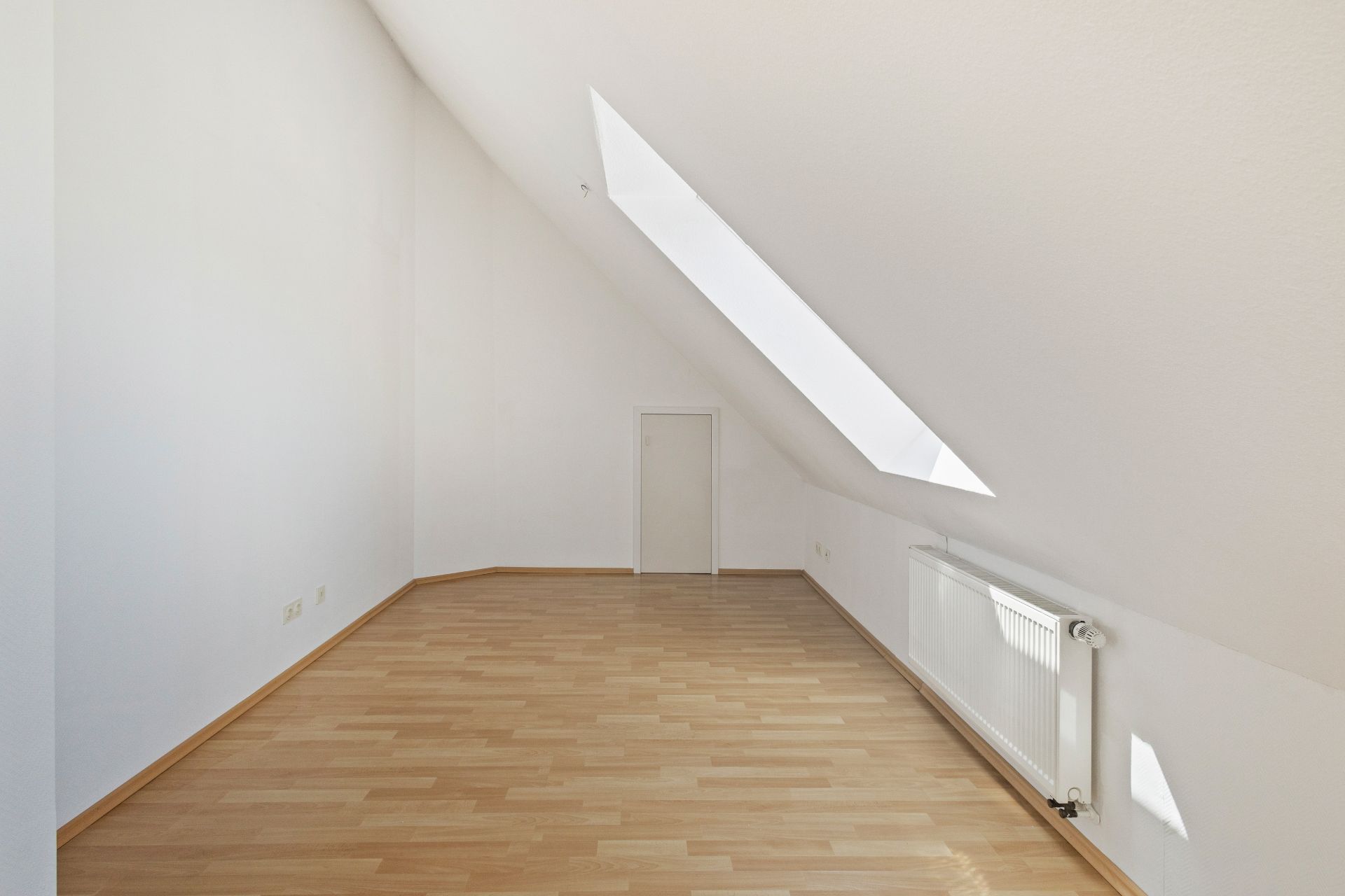 Heller Dachraum mit Laminatboden, schräger Decke und großem Dachfenster.