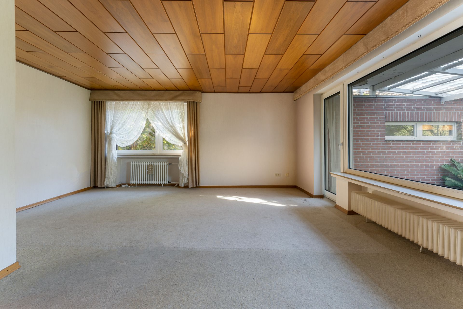 Leeres Wohnzimmer mit großem Fenster, Holzdecke und Teppichboden.