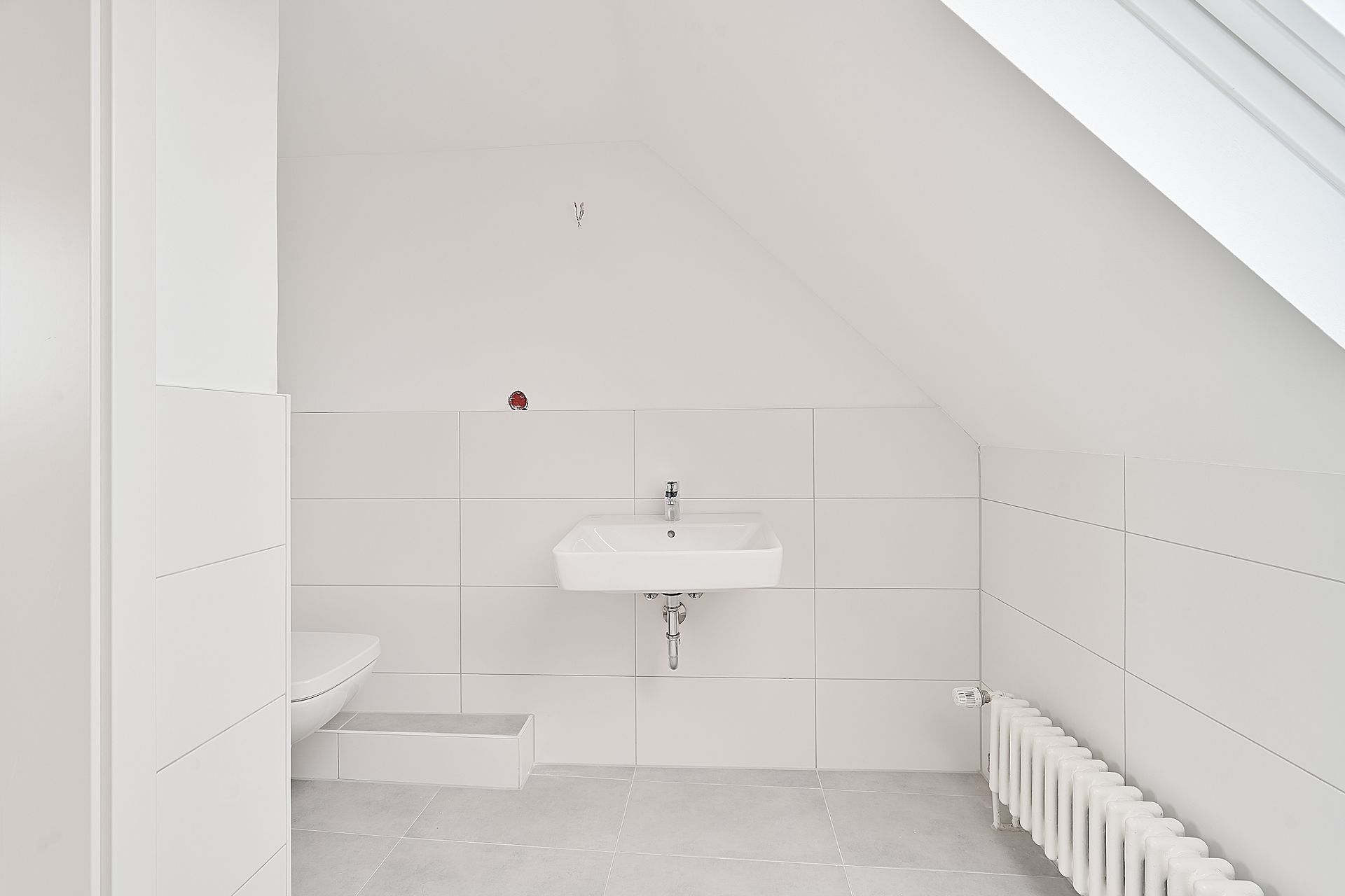 Helles Badezimmer mit Wandwaschbecken, WC und Heizkörper unter einer Dachschräge.