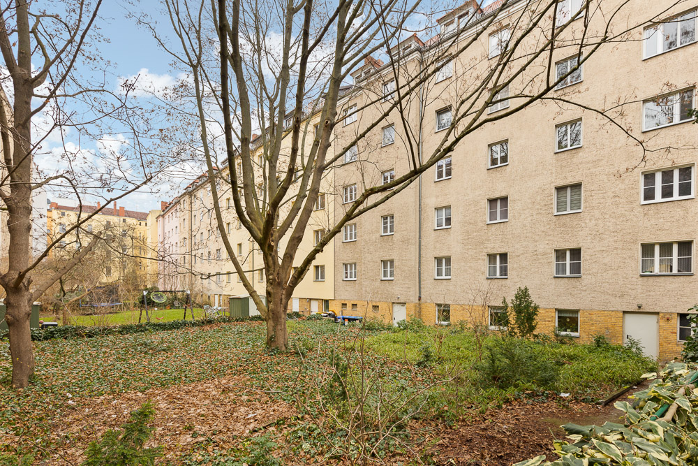 Hinterhof mit Bäumen und Sträuchern, umgeben von mehrstöckigen Wohngebäuden.