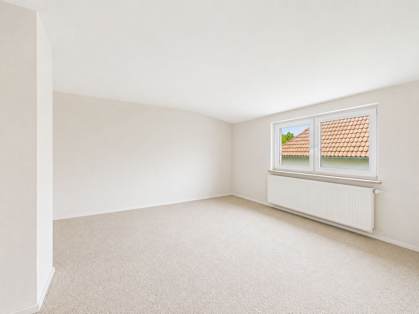 Helles, leeres Zimmer mit Teppichboden und zwei Fenstern unterhalb der Decke.