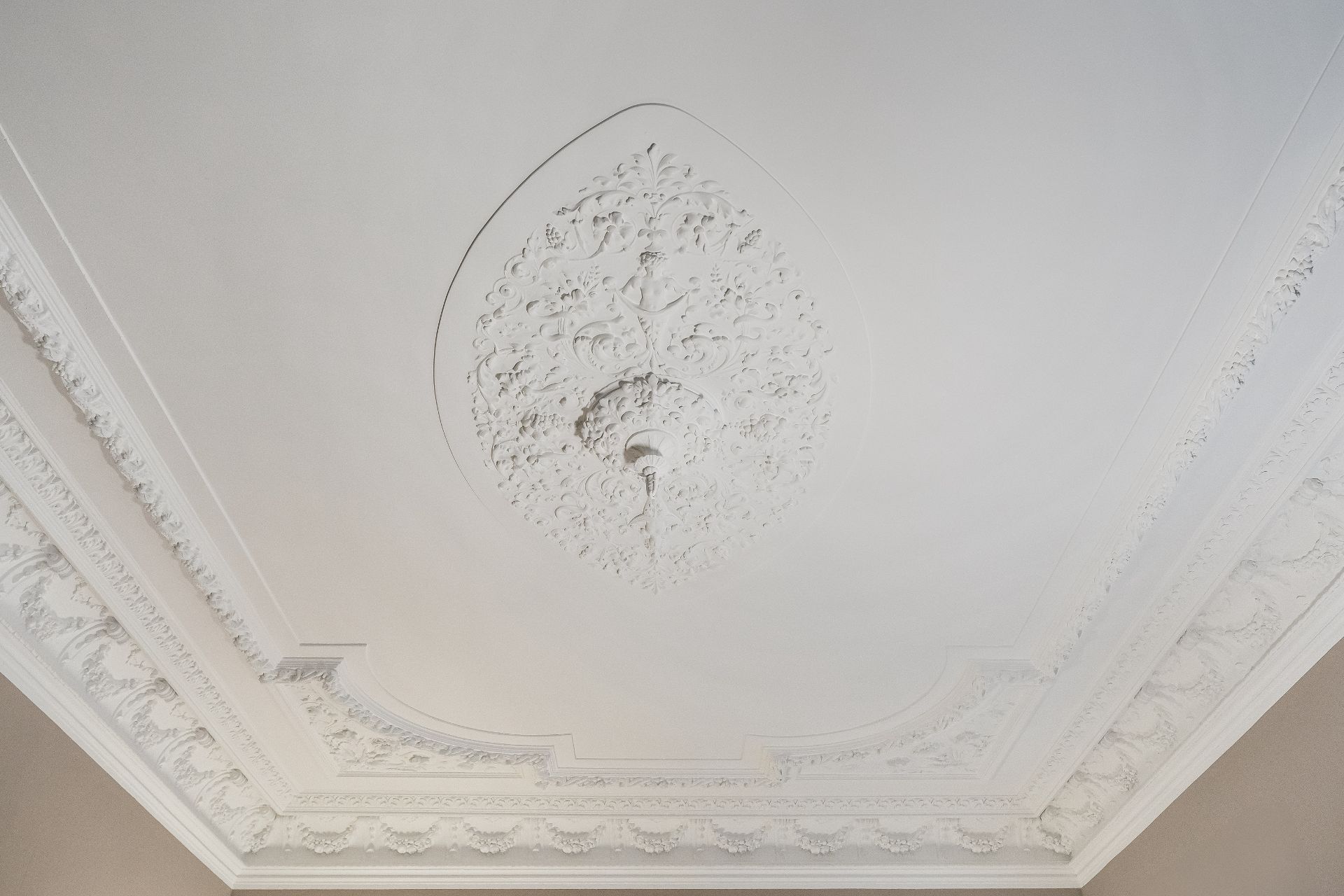 Weiße Stuckdecke mit aufwendigen Zierleisten und dekorativem Ornament in der Mitte.