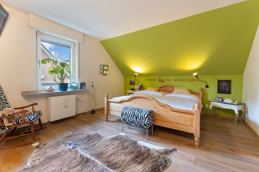 Helles Schlafzimmer mit Doppelbett, grün gestrichener Wand und Holzfußboden.