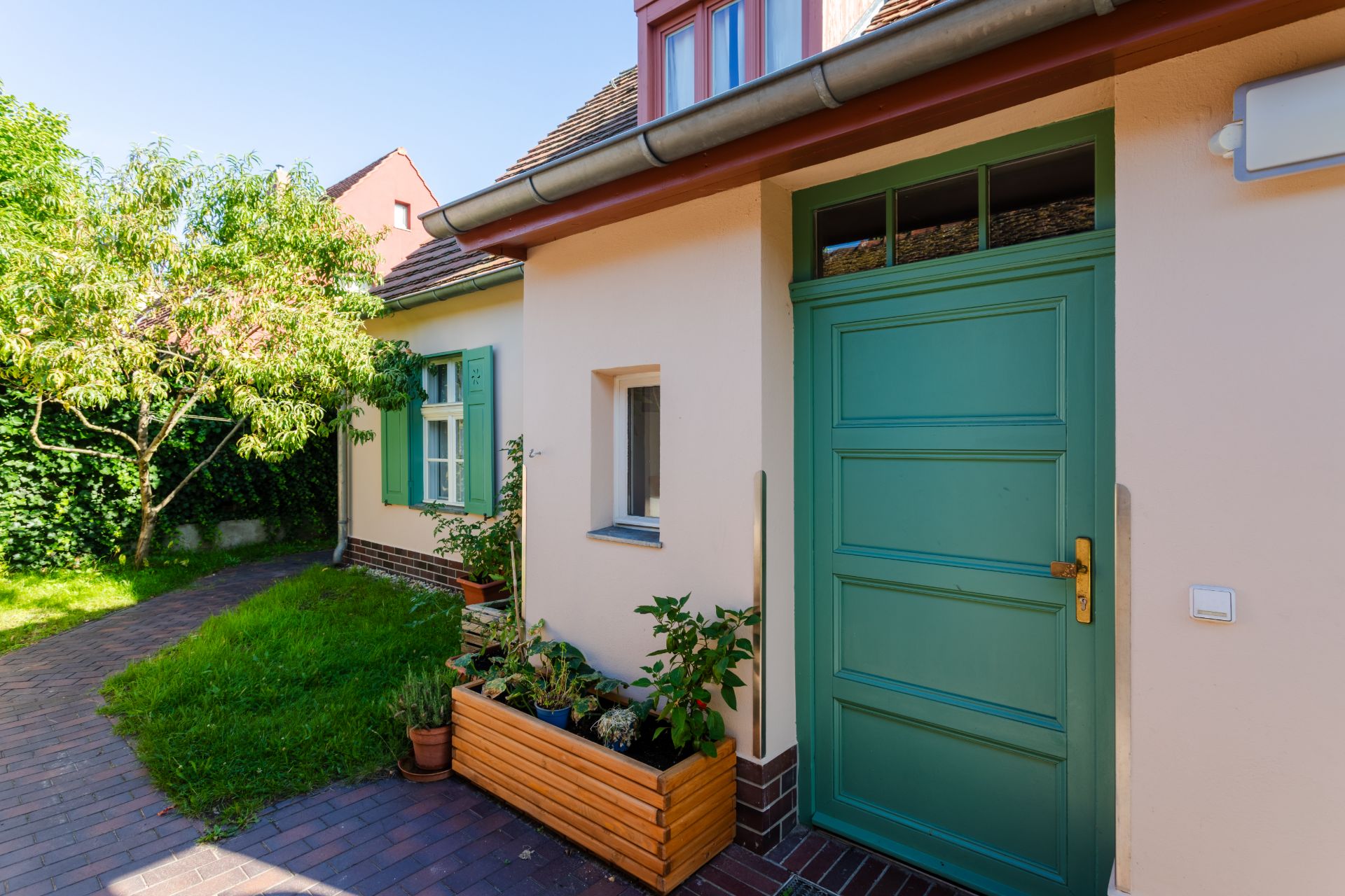 Eingang eines Hauses mit grüner Tür, Pflanzenkasten und Fenster mit grünen Fensterläden.