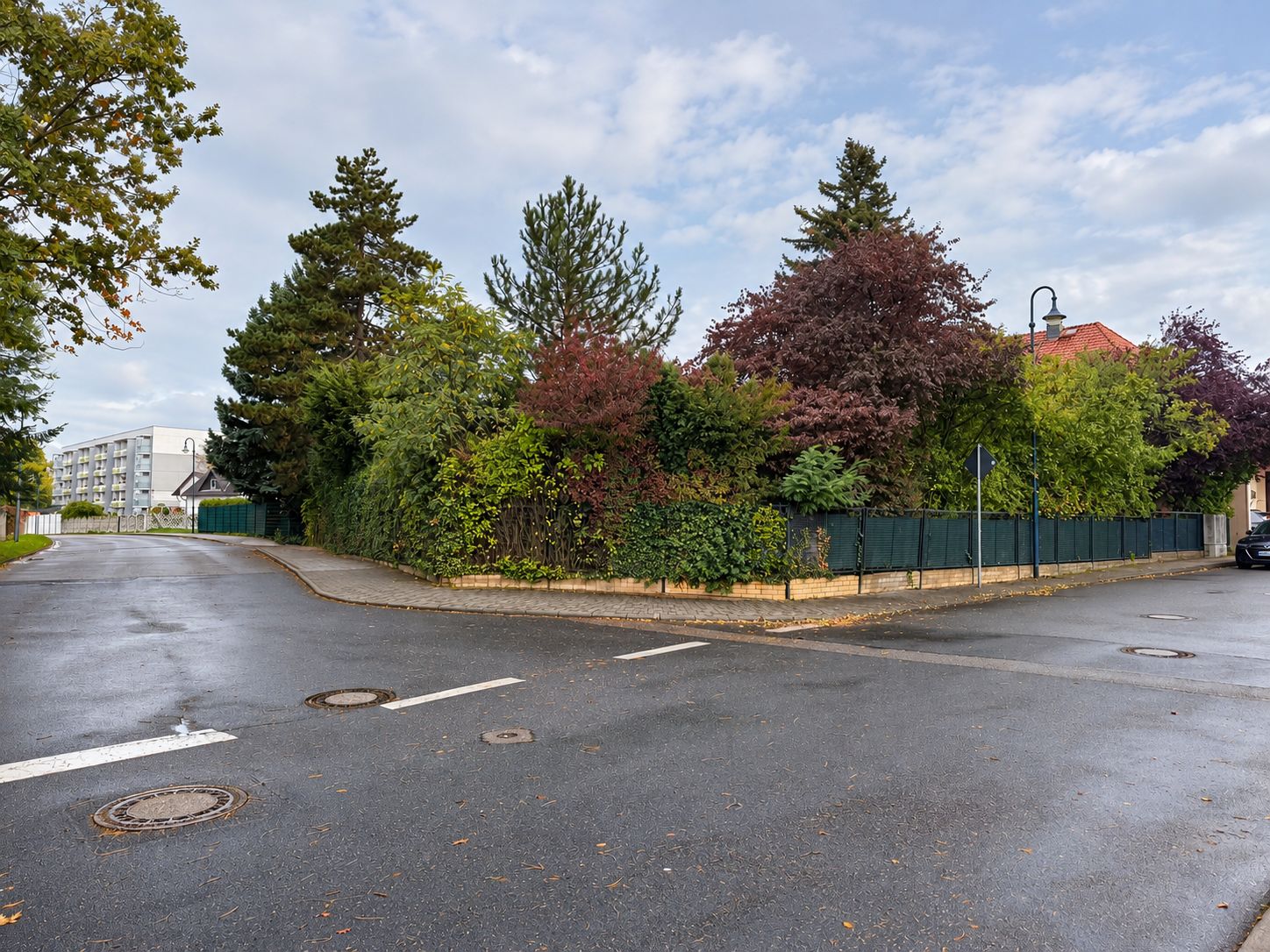 Ecke eines Wohnviertels mit Zaun und dichter Bepflanzung entlang des Gehwegs.