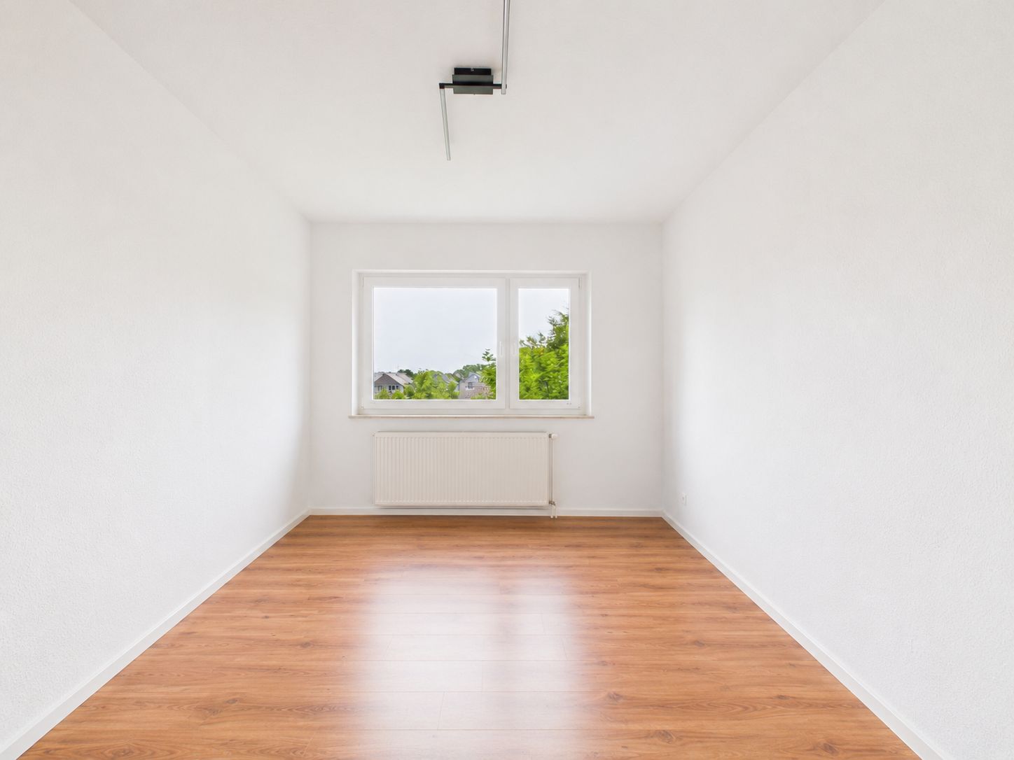 Leerer, heller Raum mit weißem Wänden, Holzfußboden und Fenster mit Blick ins Grüne.