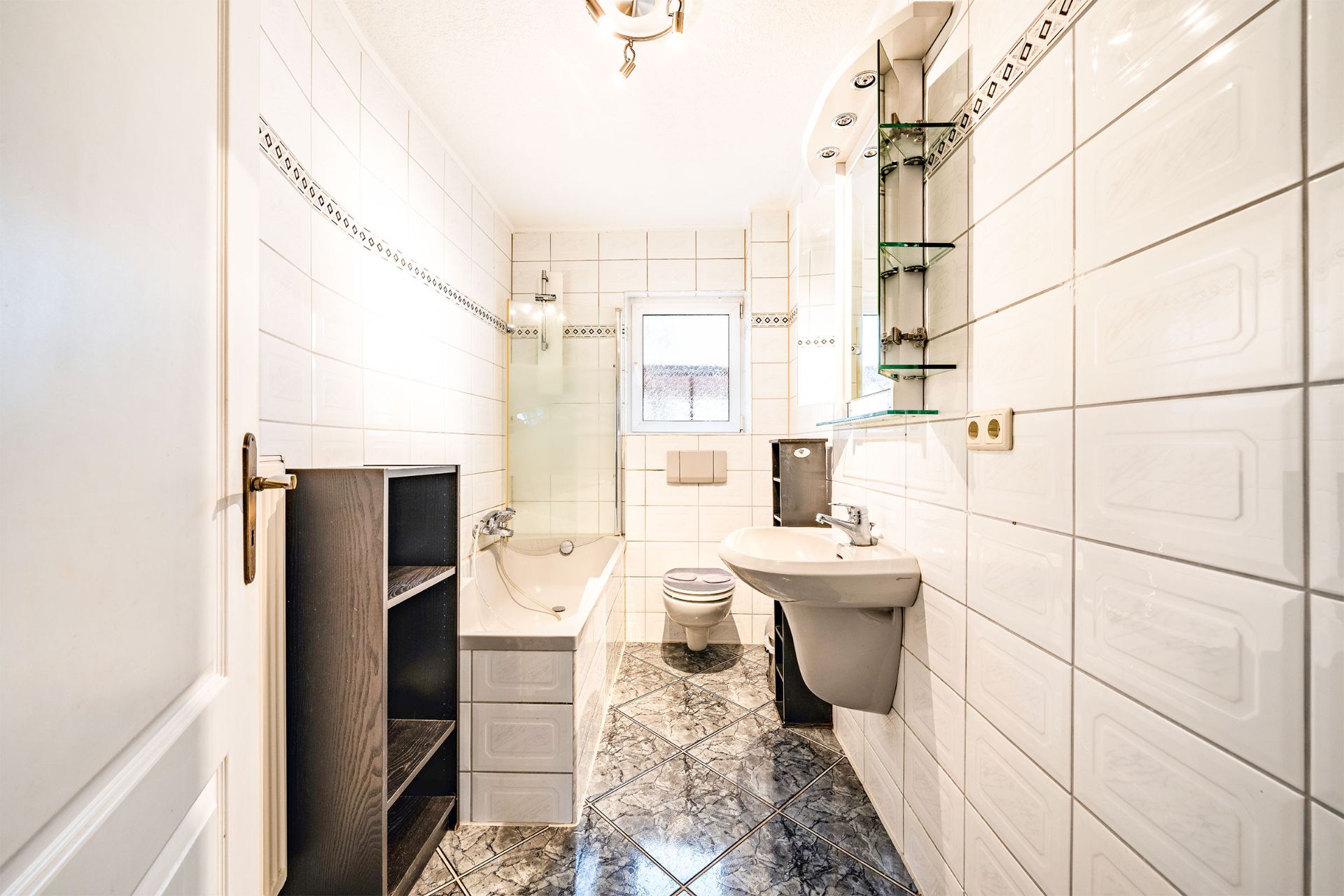 Helles Badezimmer mit Badewanne, Waschbecken, Toilette und Regal, weiß gefliest.