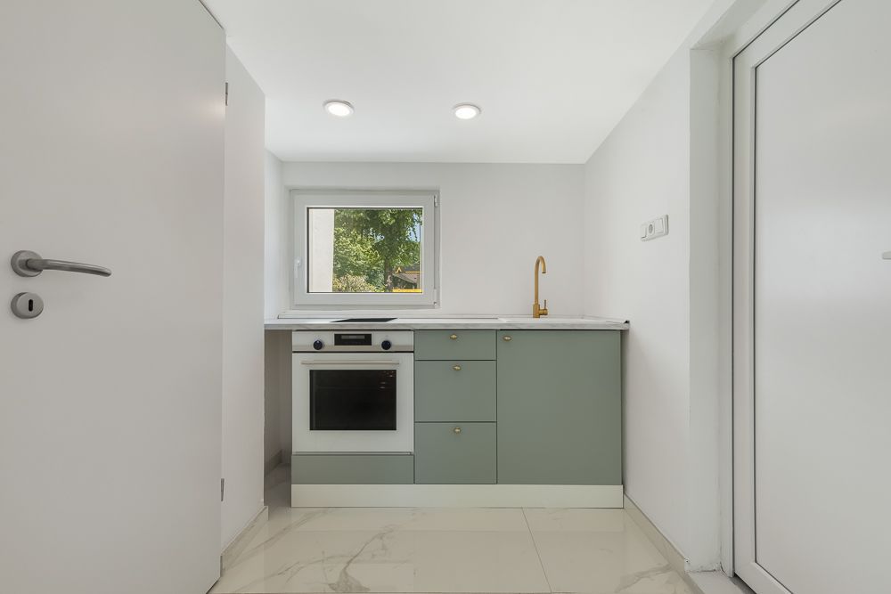 Kleine moderne Küche mit grünem Unterschrank, Ofen, Fenster und goldener Armatur.