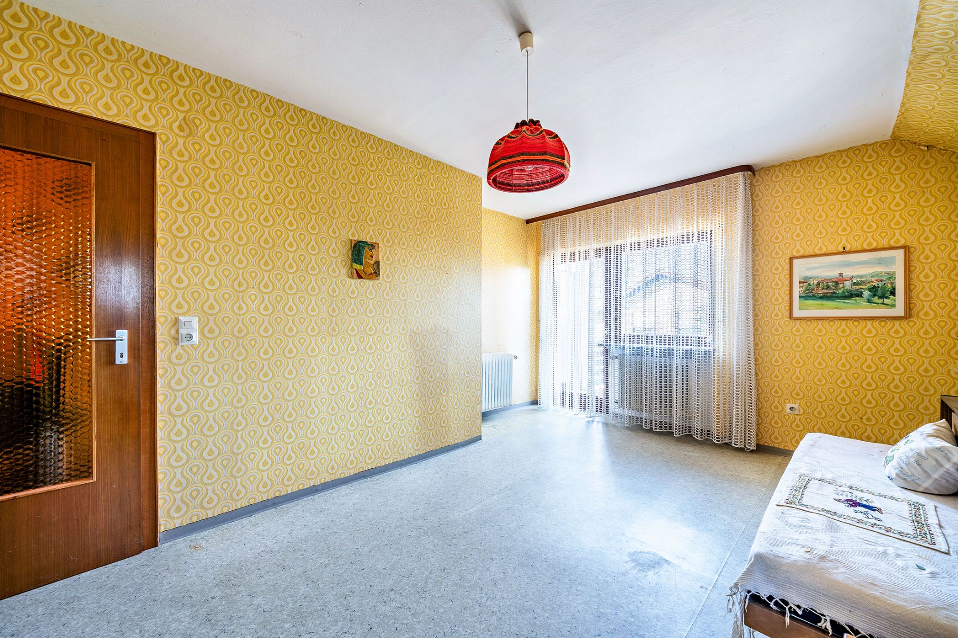 Helles Wohnzimmer mit gelber Tapete, einem Sofa, roter Lampe und Tür mit Glas.