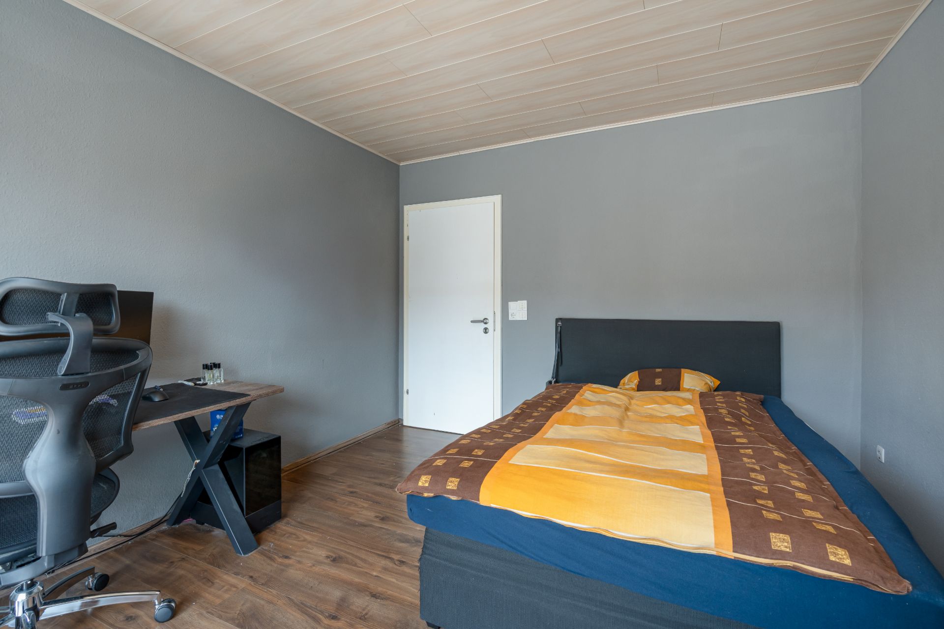 Schlafzimmer mit Einzelbett, Schreibtisch, Bürostuhl und Holzboden.