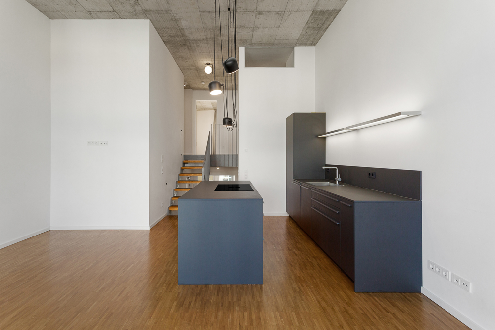 Moderne Küche mit dunklen Schränken, Kochinsel und Holzfußboden, dahinter Treppe nach oben.