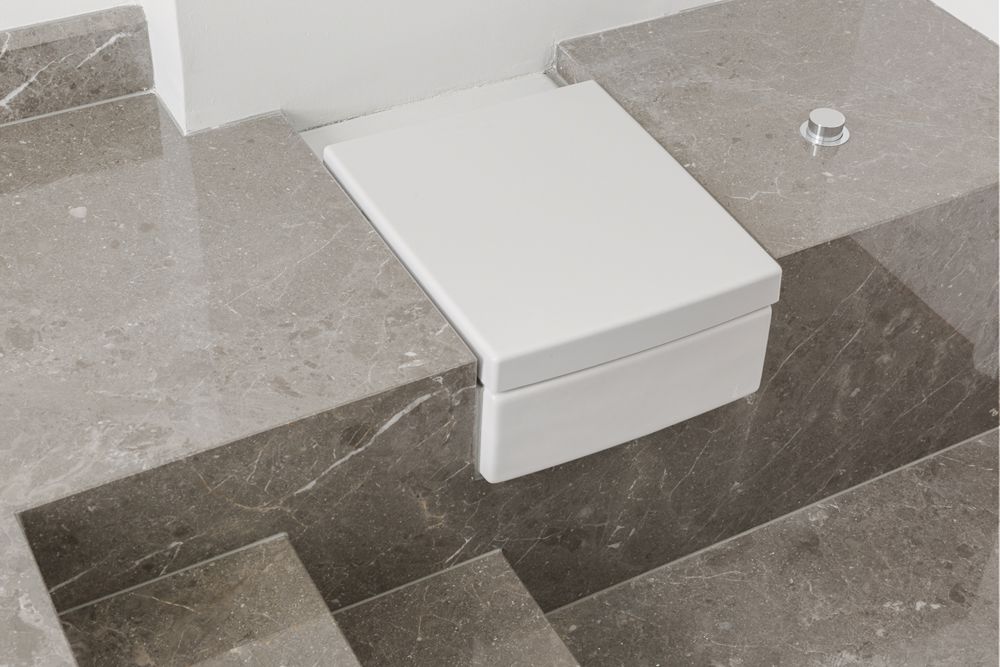 Eine moderne, wandhängende Toilette mit geschlossenem Deckel auf grauen Marmorfliesen.