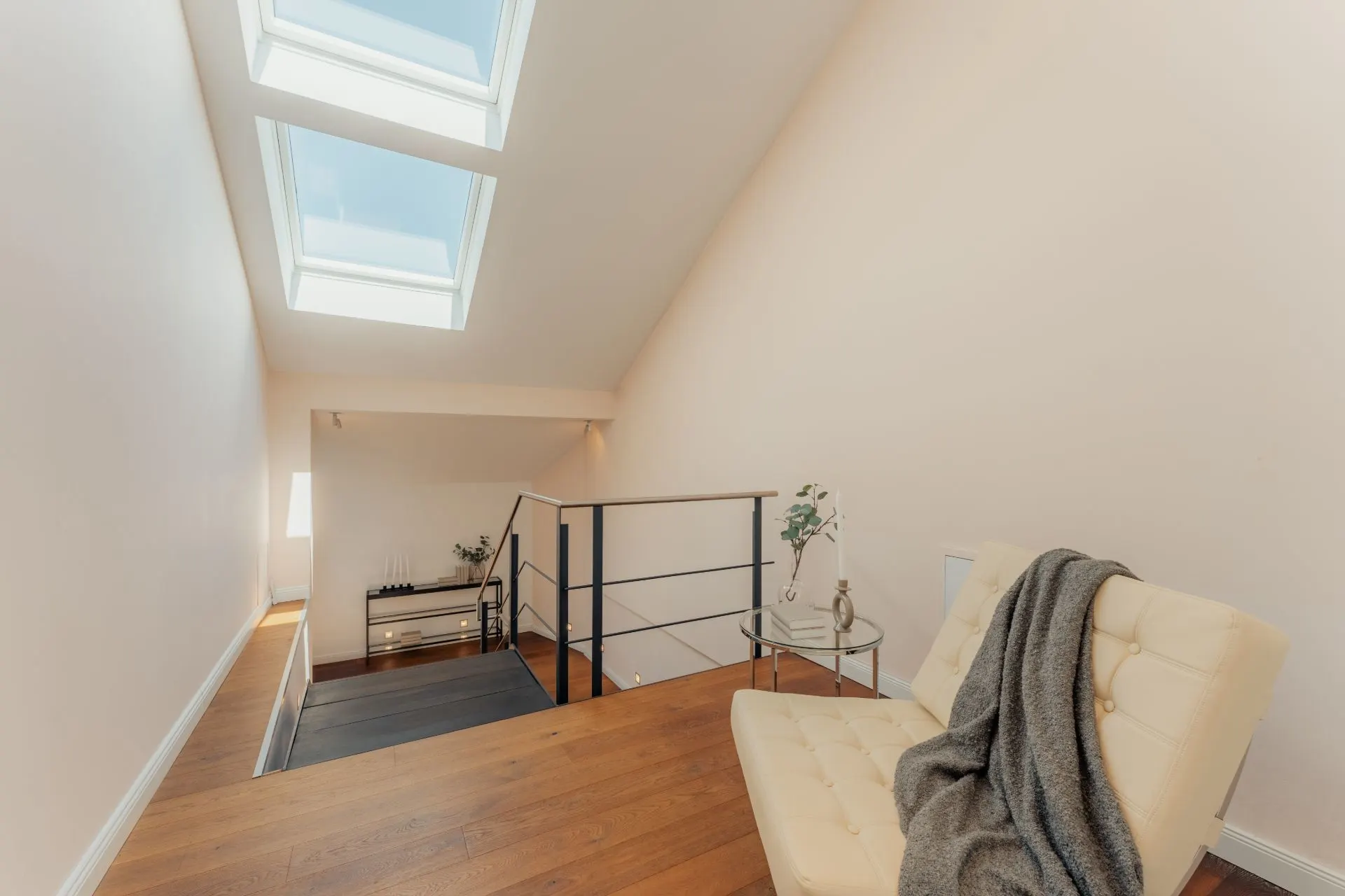 Heller Wohnbereich mit Dachfenstern, Treppe, Sessel und kleinem Tisch mit Pflanze.