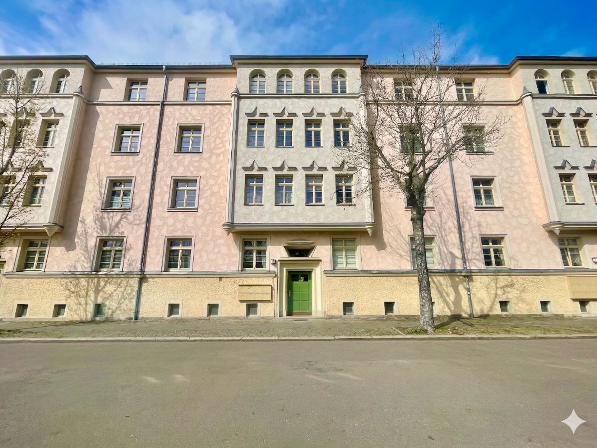 Mehrstöckiges Wohngebäude mit grünem Eingang und mehreren Fenstern an einer ruhigen Straße.