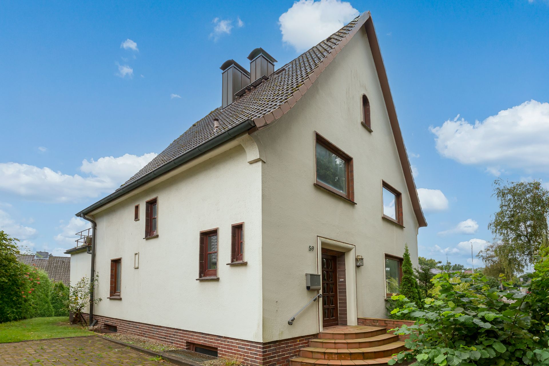 Zweistöckiges Einfamilienhaus mit Satteldach, helle Fassade und roten Fensterrahmen.