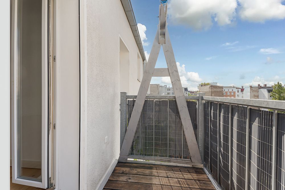 Schmaler Balkon mit Holzfußboden und offenem Zugang, Blick auf Stadt und Himmel.