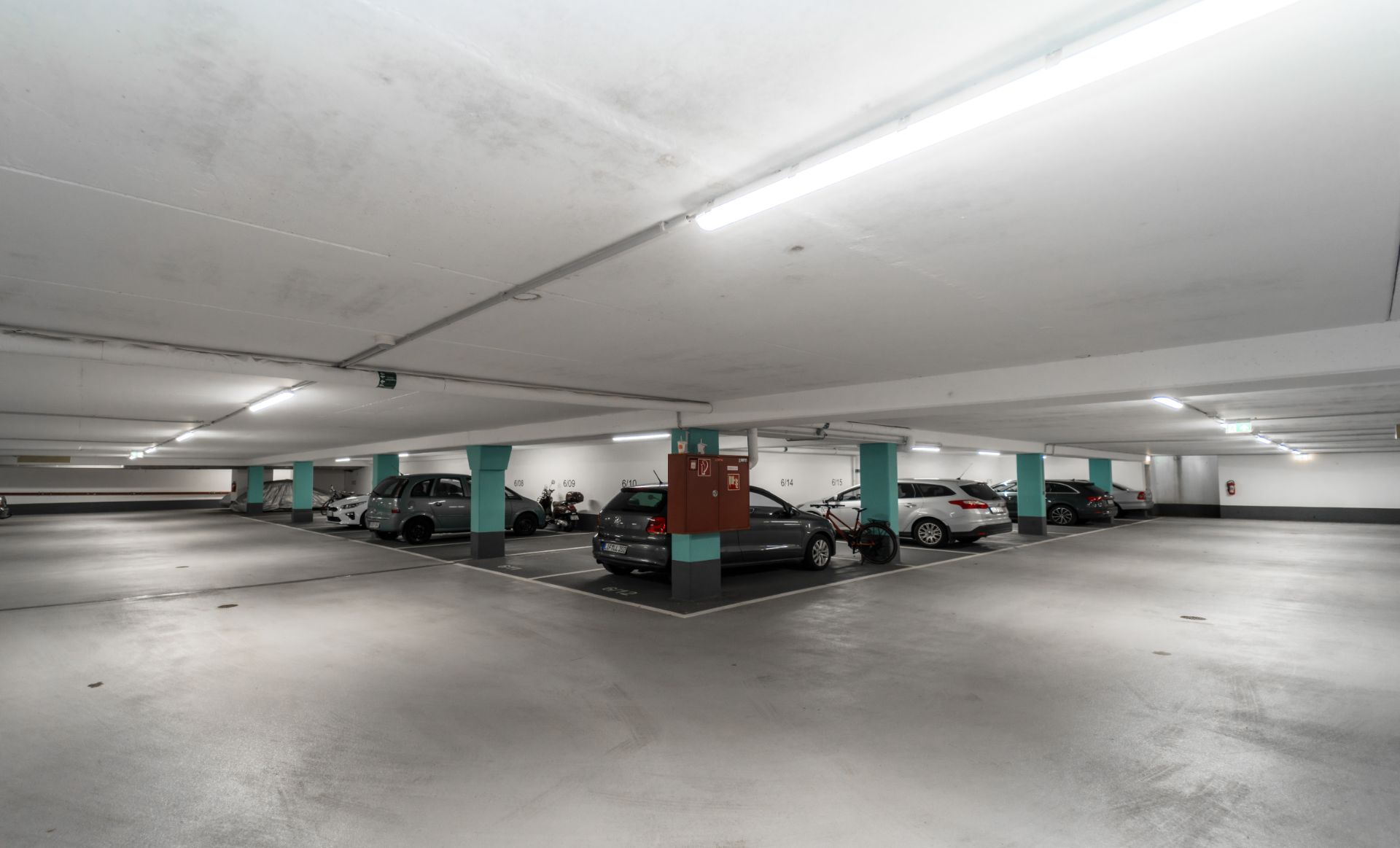 Tiefgaragenparkplatz mit geparkten Autos und beleuchteten Deckenleuchten.