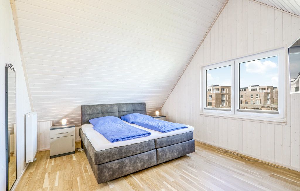 Schlafzimmer mit Doppelbett, blauer Bettwäsche, Nachttischen und großem Fenster unter Dachschräge.