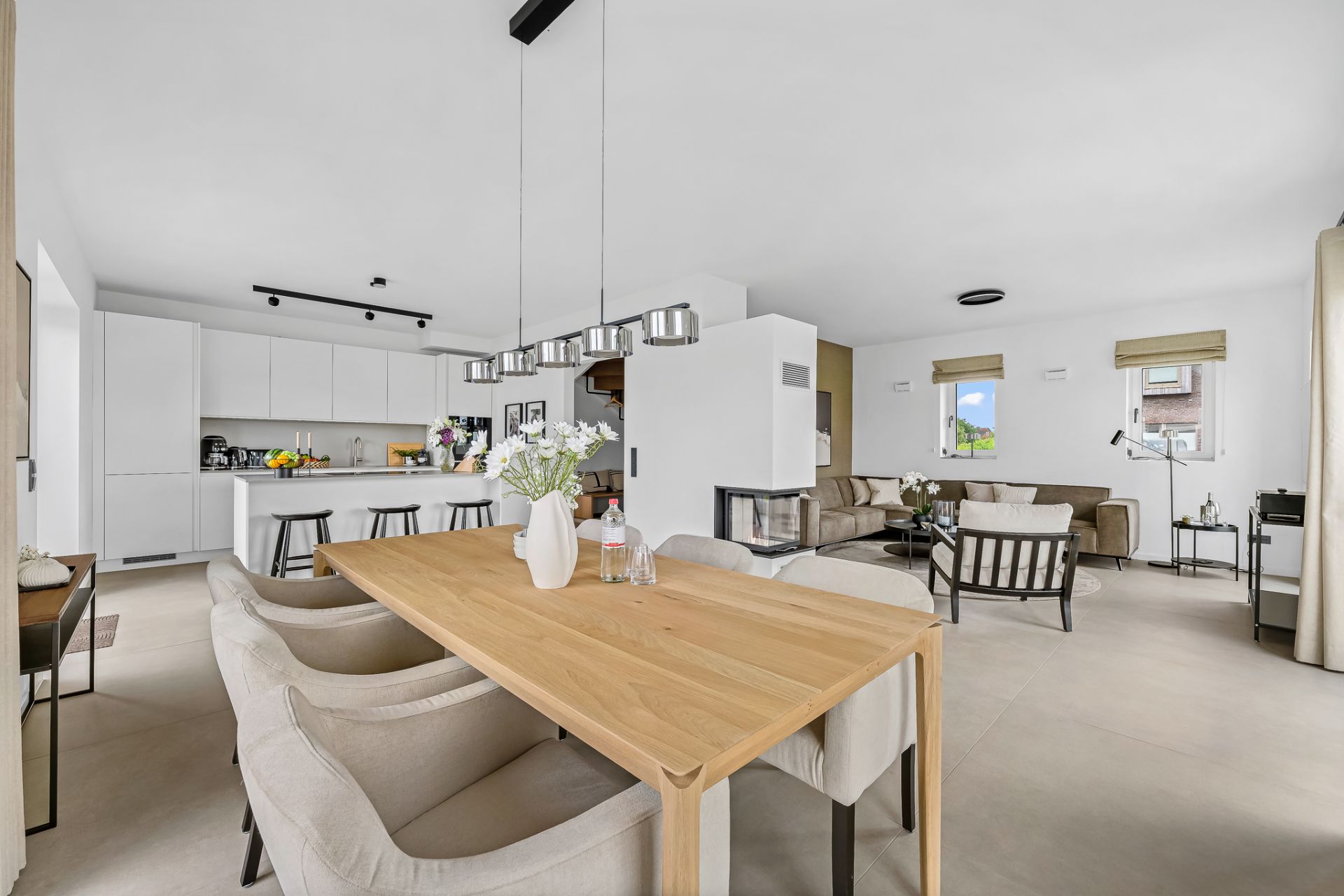 Modernes, offenes Wohn- und Esszimmer mit Holztisch, Küche im Hintergrund.