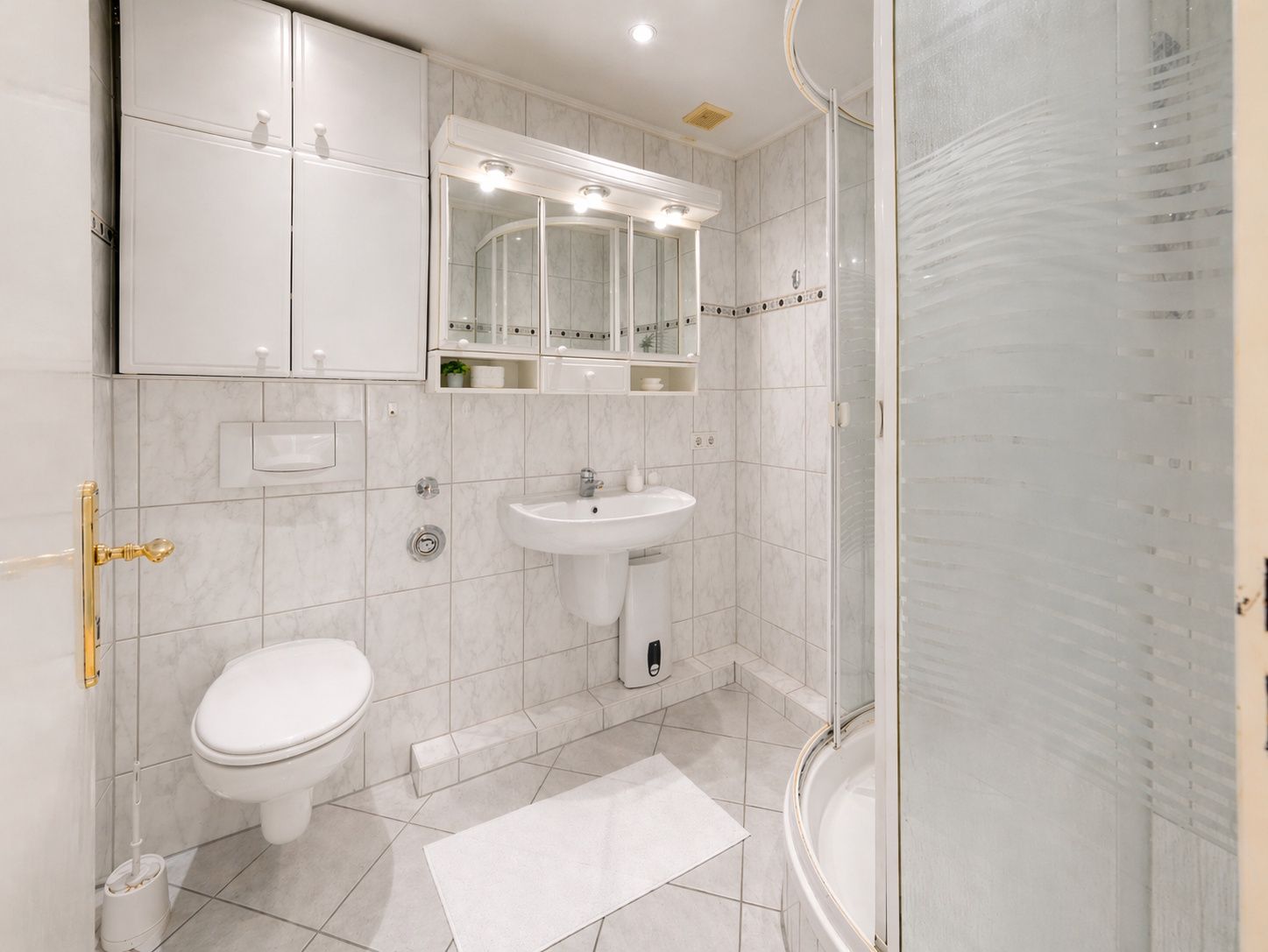 Helles Badezimmer mit Dusche, WC, Waschbecken und Spiegelschrank.