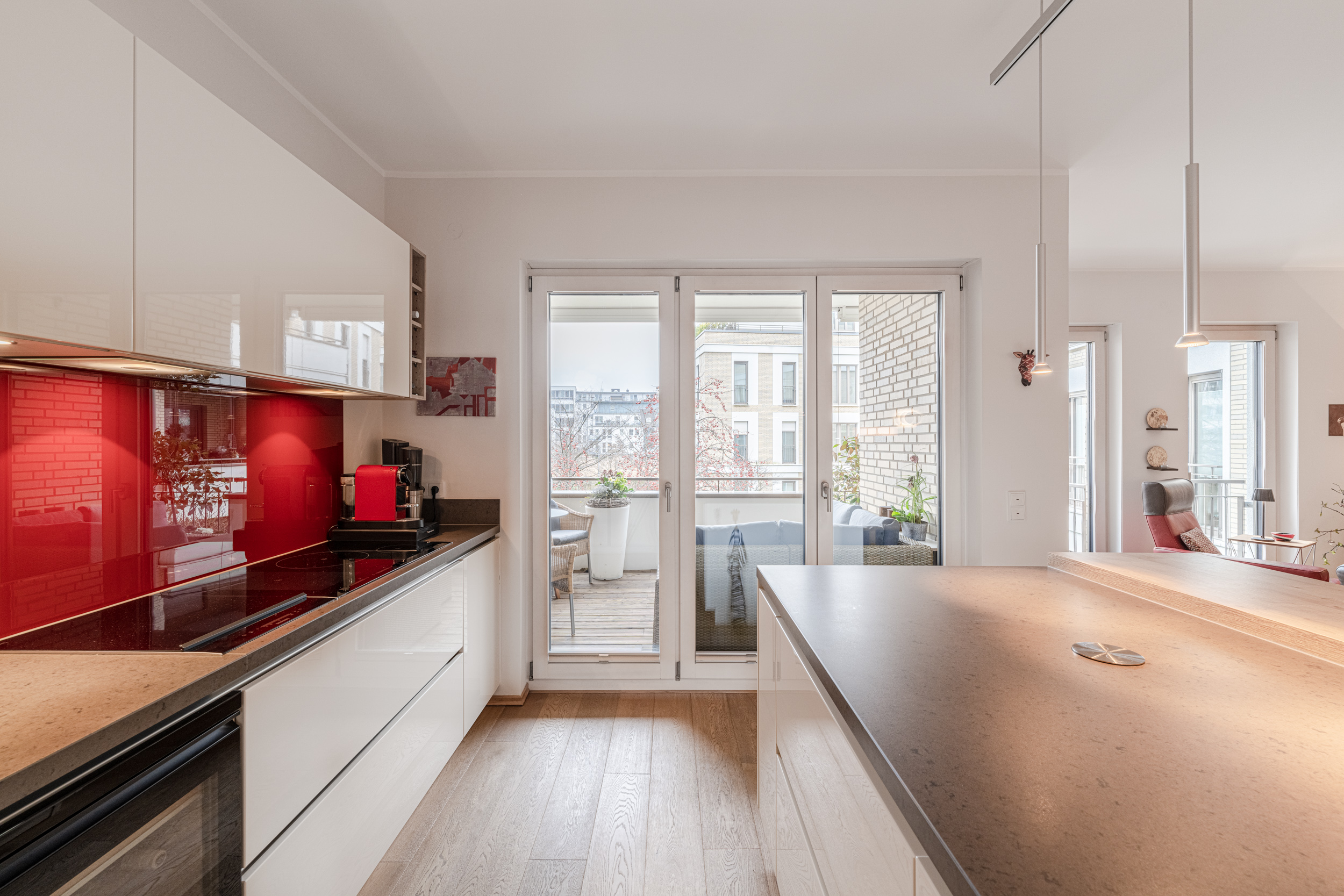 Moderne Küche mit rotem Spritzschutz und Zugang zum Balkon mit Sitzbereich.