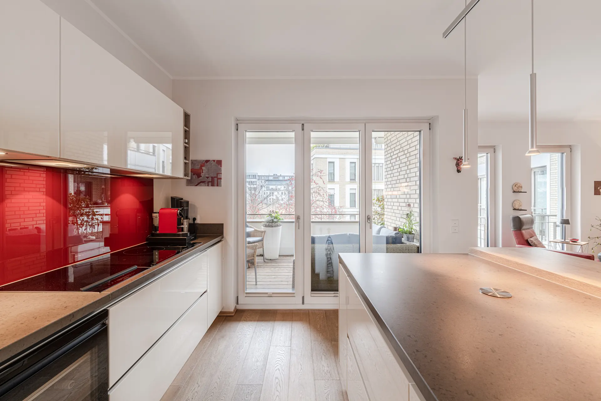 Moderne Küche mit rotem Spritzschutz und Zugang zum Balkon mit Sitzbereich.