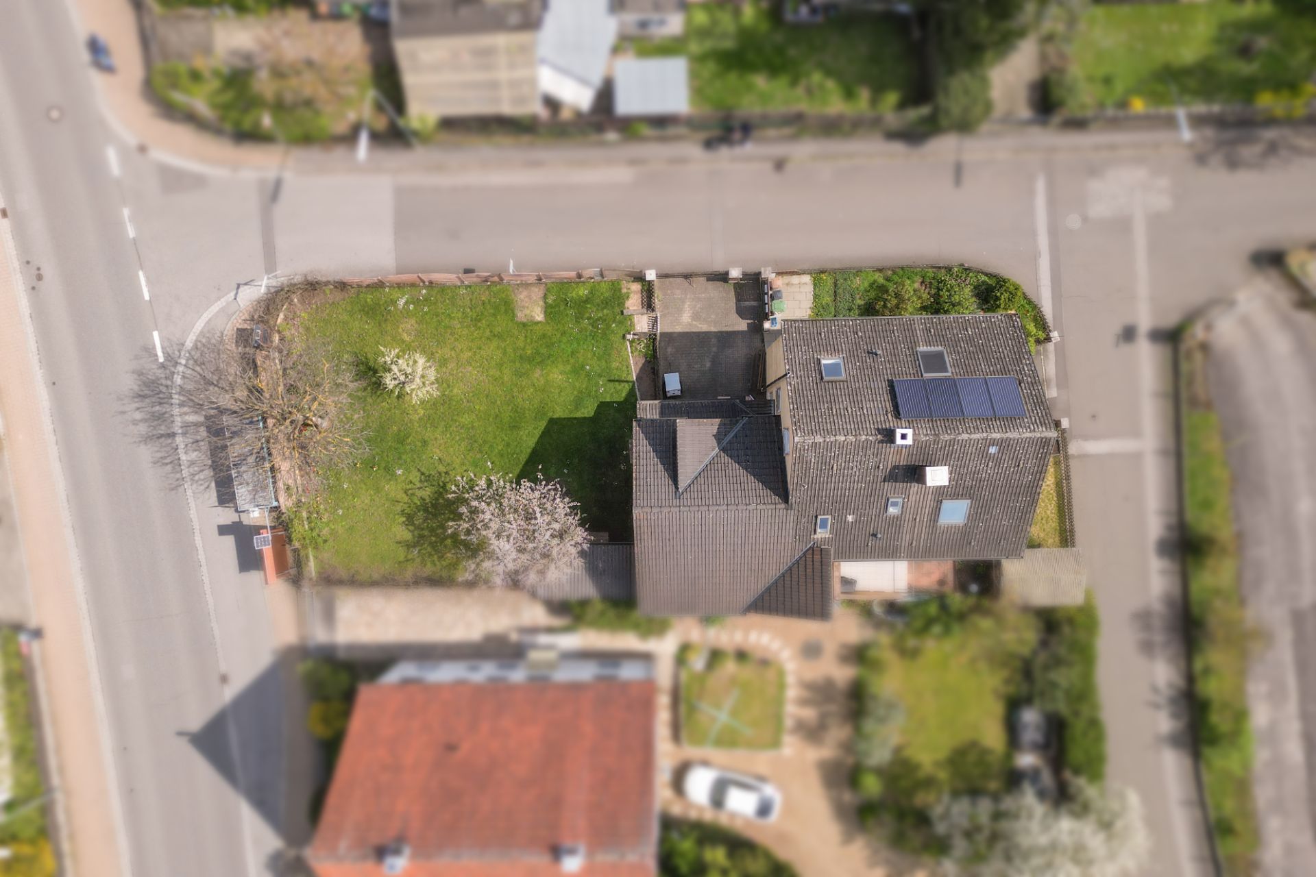 Luftaufnahme eines Hauses mit Garten an einer Straßenecke.