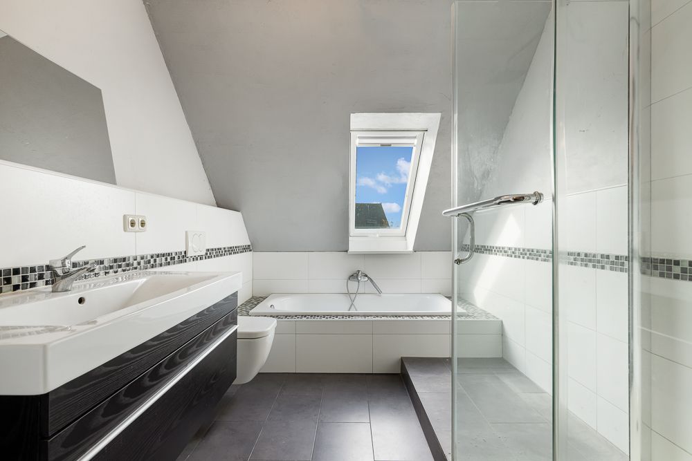 Modernes Badezimmer mit Waschbecken, Toilette, Badewanne, Dusche und Fenster im Dachgeschoss.