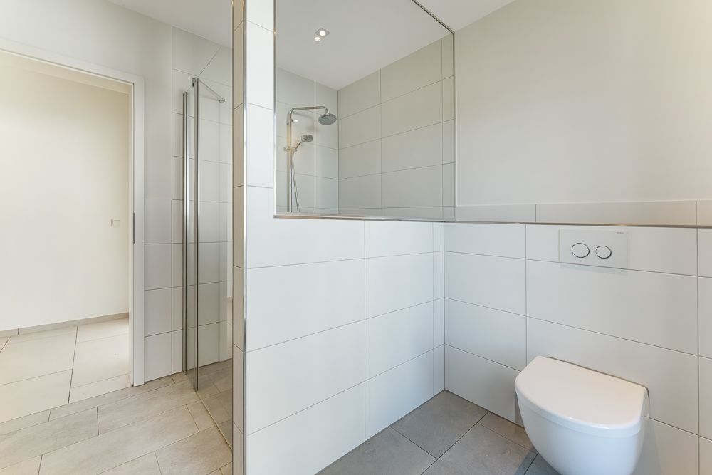 Modernes Badezimmer mit offener Dusche und Wandtoilette, helle Fliesen an Wand und Boden.