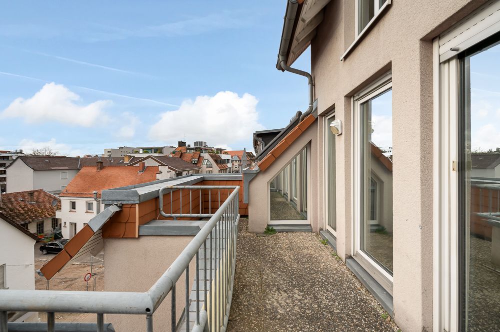 Balkon mit Metallgeländer an einem Wohngebäude, Blick auf Nachbarhäuser und blauen Himmel.