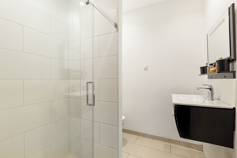 Modernes Badezimmer mit Glasduschkabine, Waschbecken, Spiegel und weißen Fliesen.