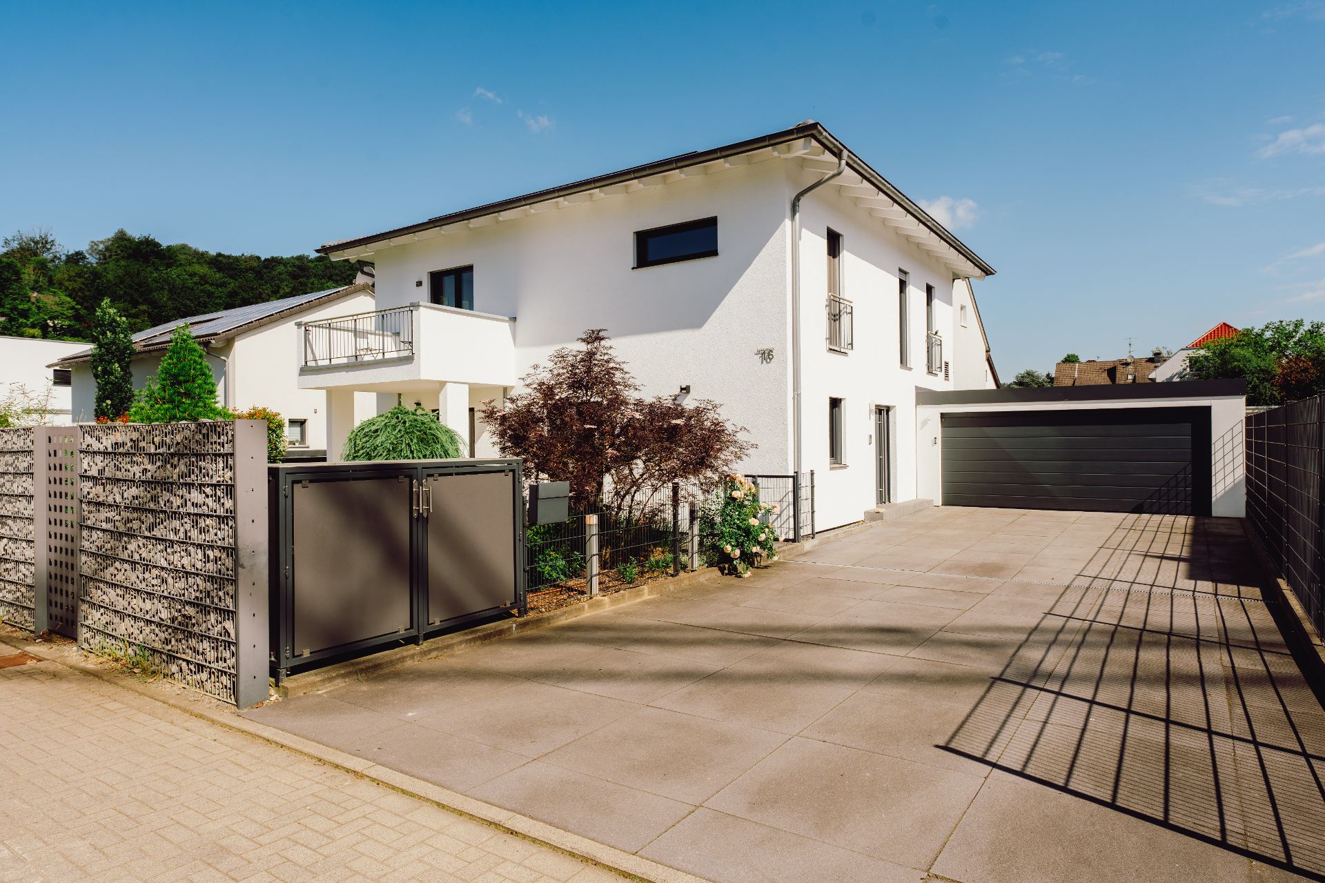 Modernes weißes Wohnhaus mit Doppelgarage, Einfahrt und Garten, umgeben von Zaun.