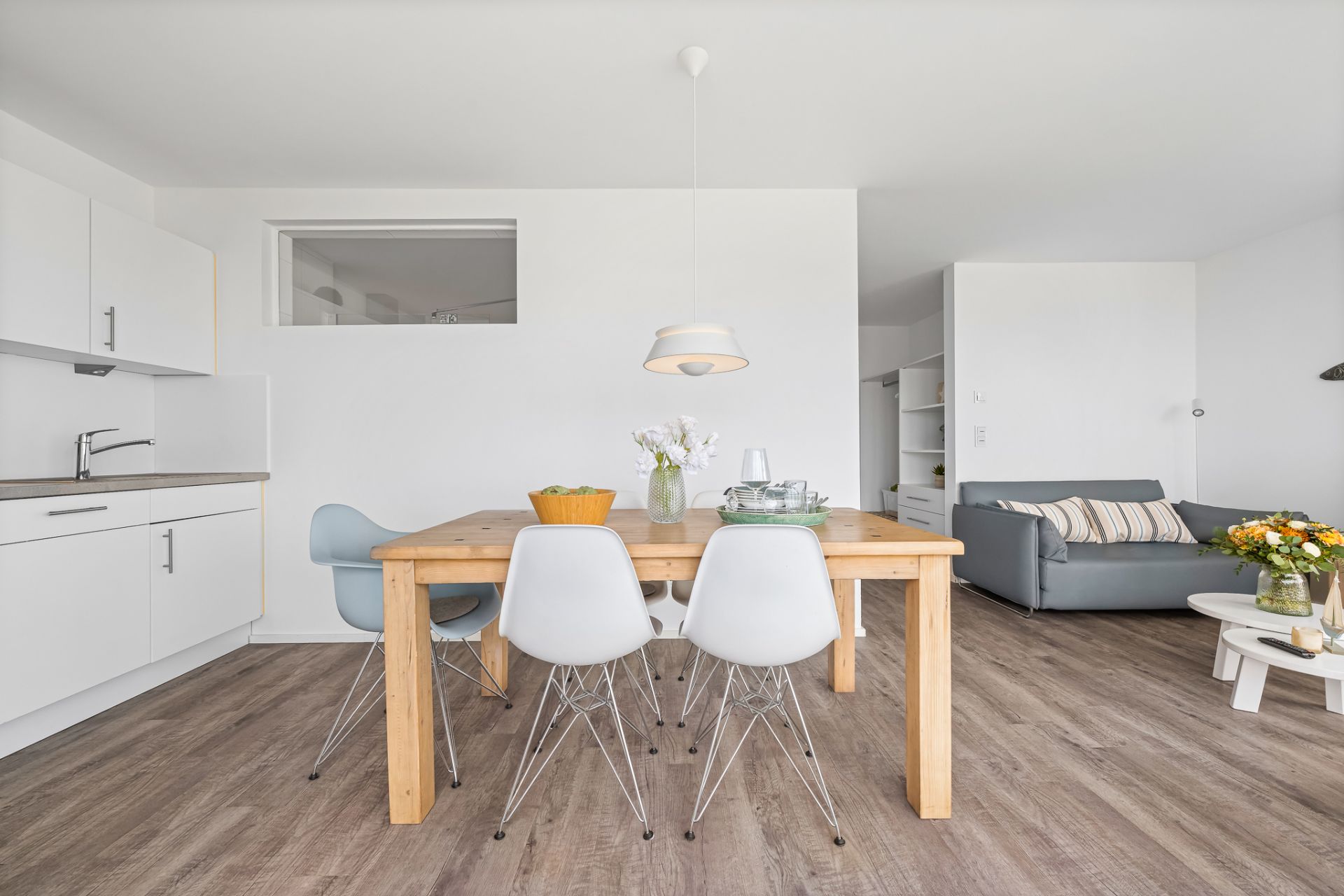 Heller Raum mit Esstisch, vier Stühlen, Küche links und Sofa im Hintergrund.