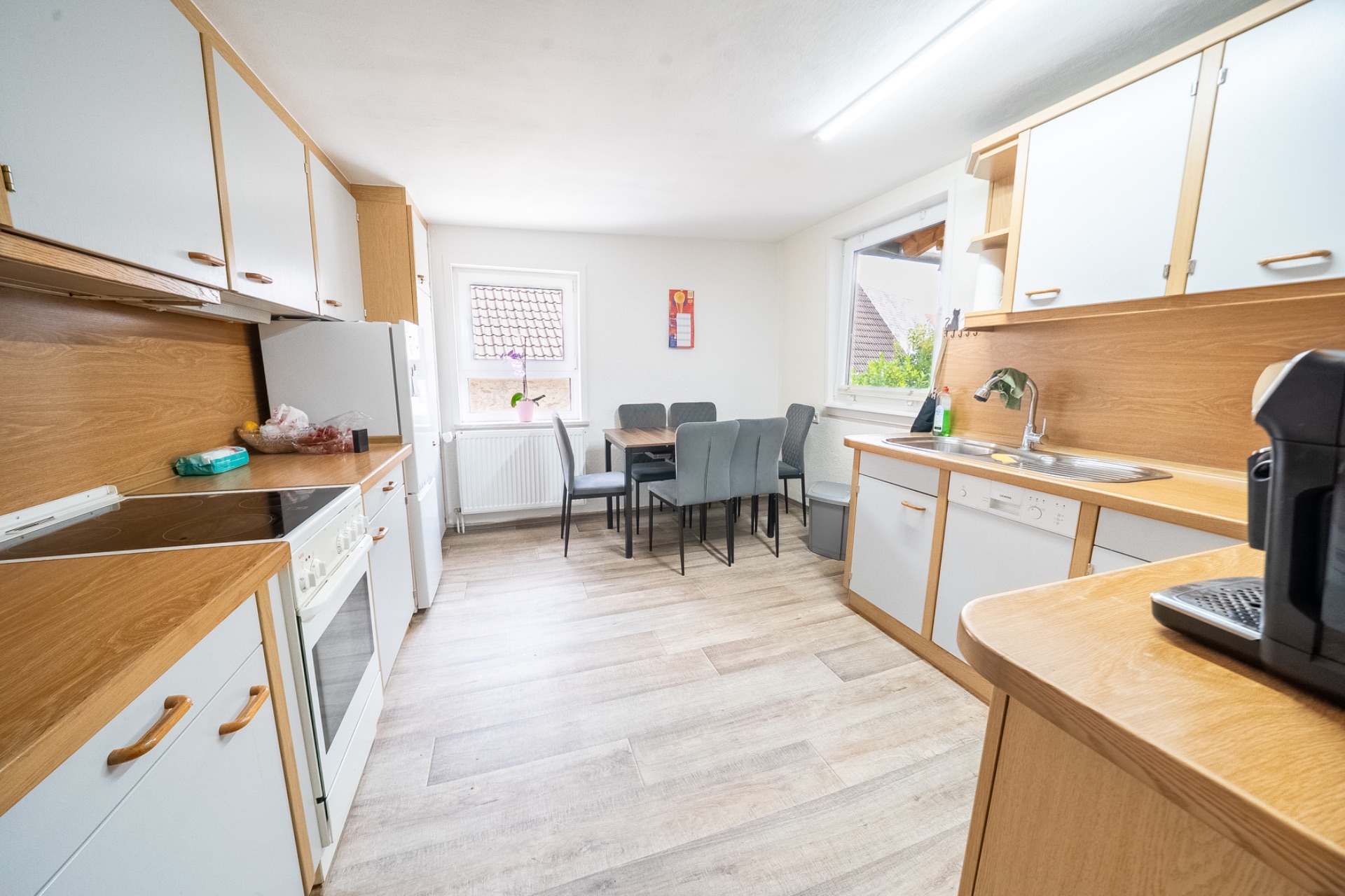 Helle Küche mit Holzfronten, Esstisch und sechs Stühlen, großer Fenstern und moderner Ausstattung.