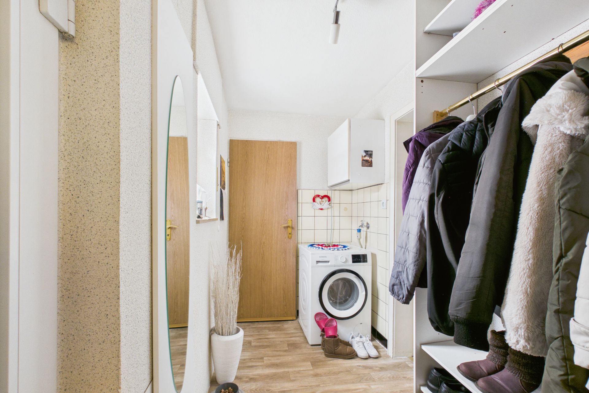 Flur mit Garderobe, Spiegel, Waschmaschine und Holztür in einer Wohnung.