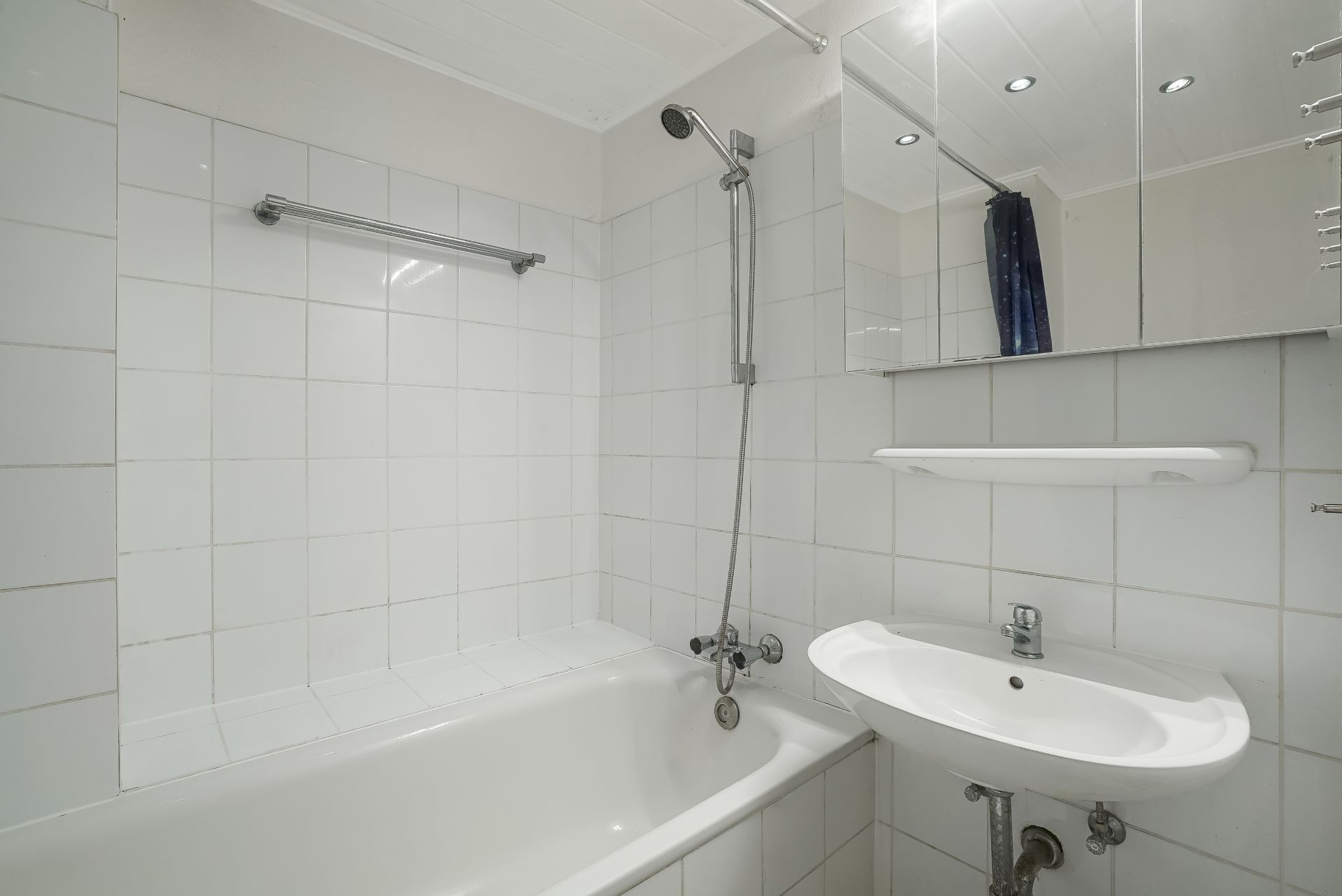 Weiß gefliestes Badezimmer mit Badewanne, Dusche, Waschbecken und Spiegel.
