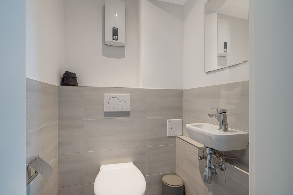 Modernes kleines Badezimmer mit Toilette, Waschbecken, Spiegel und Mülleimer.